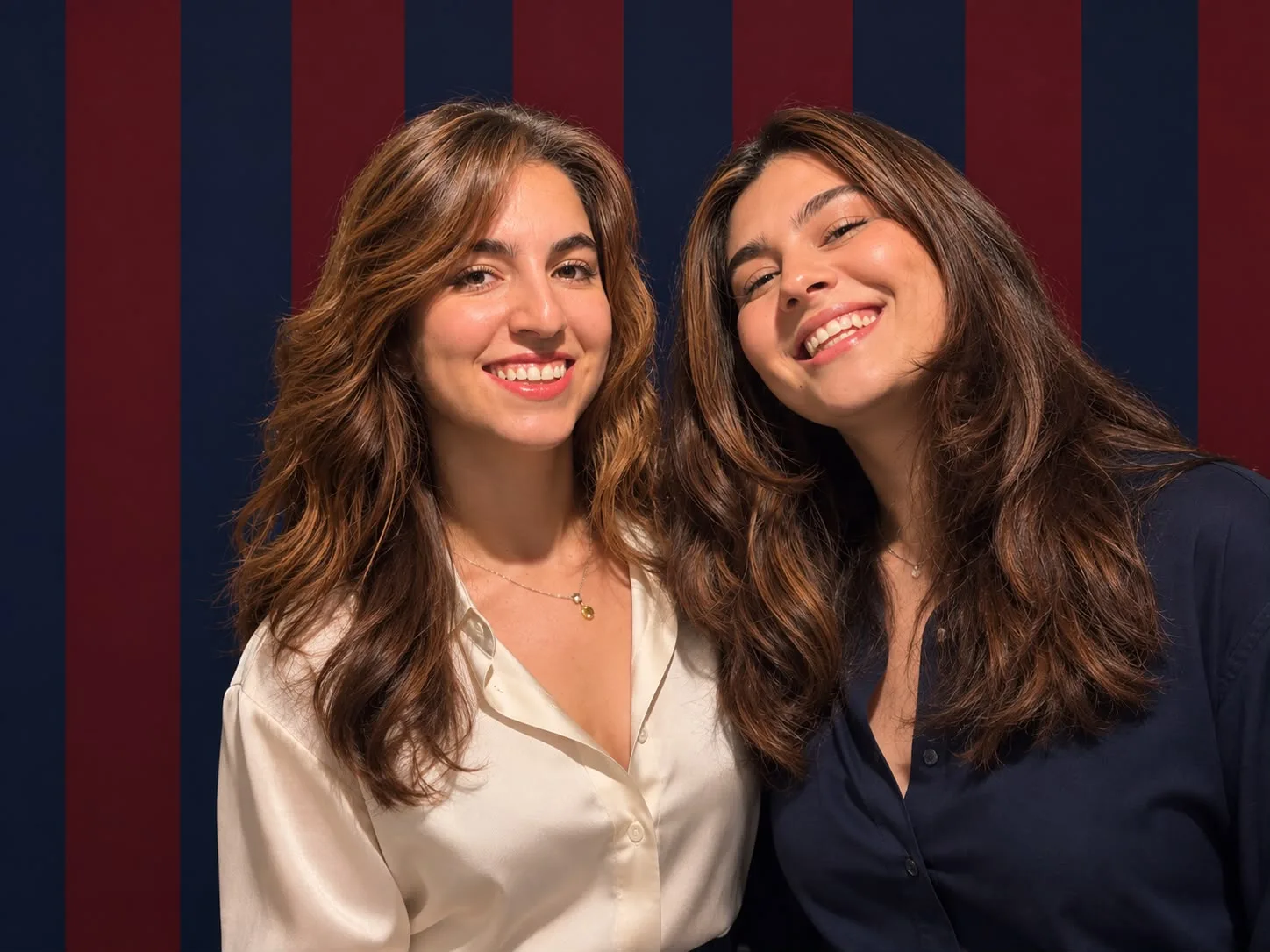 Kurucu öğretmenler Deniz ve Yasemin, bordo ve lacivert çizgili fonun önünde gülümsüyor